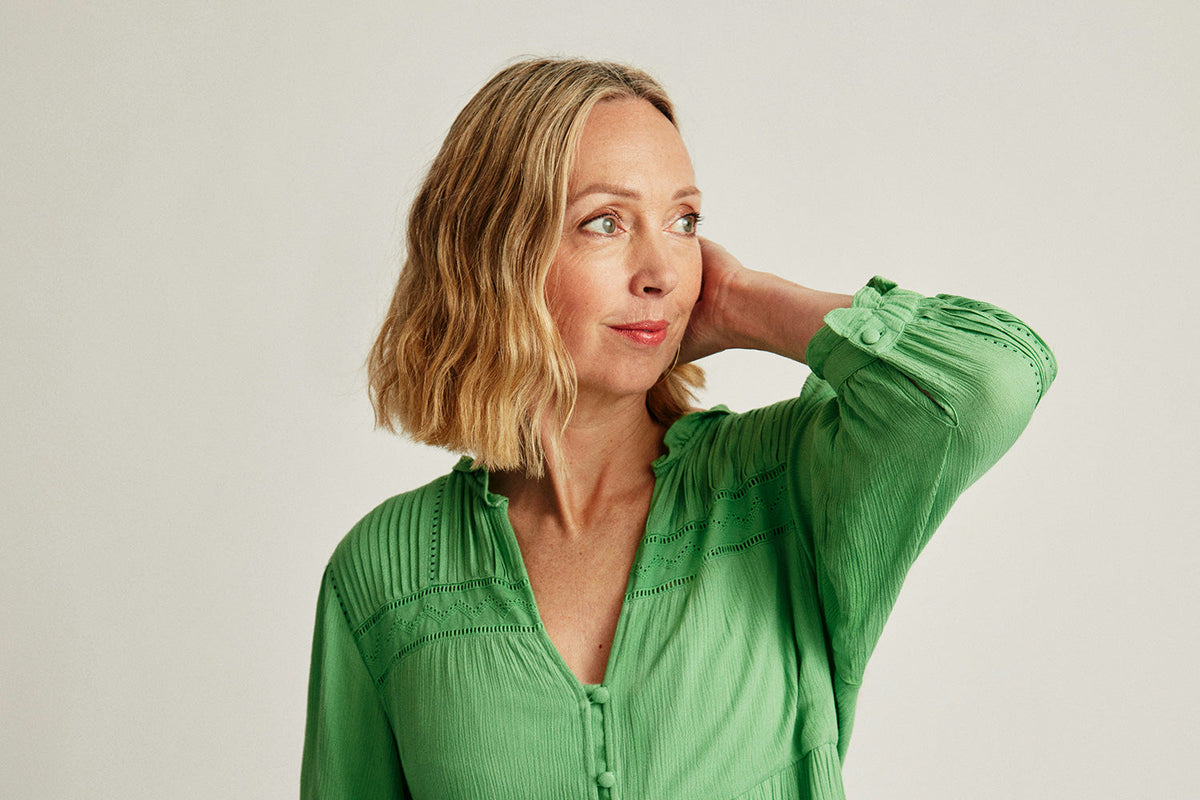 Image of older woman in green dress with hand near head