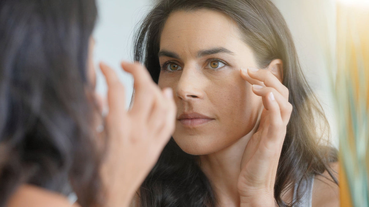 Woman looking into mirror, touching cheek with hand