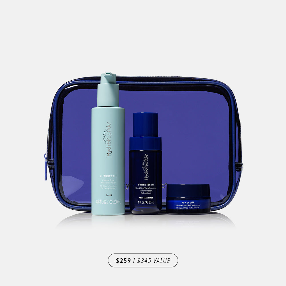 Three skincare products in front of a blue travel bag on a light gray background
