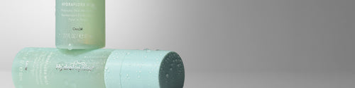 Two pale mint green HydroPeptide HydraFlora Mist bottles, arranged on a neutral gray studio background.