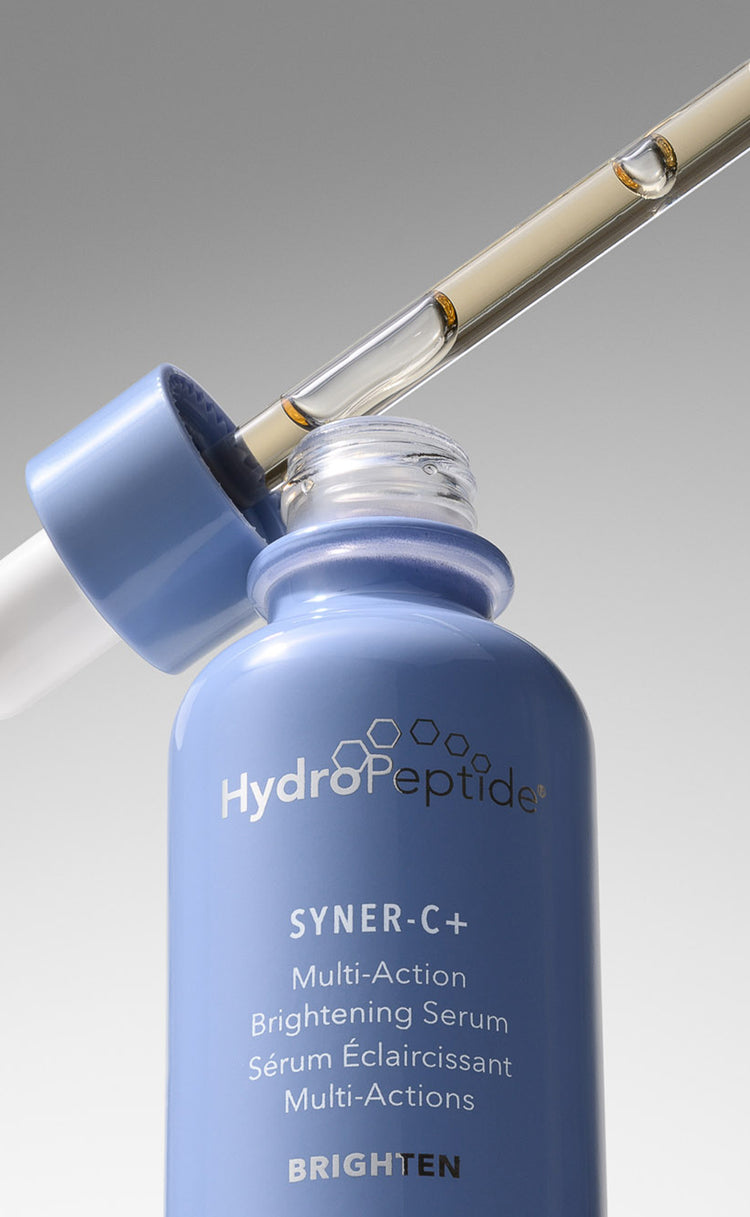 HydroPeptide Syner+C bottle with dropper filled with light gold liquid, on a light grey background.
