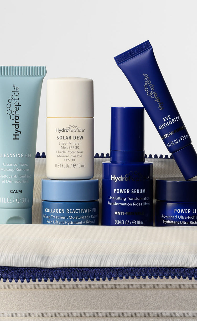 A set of HydroPeptide skincare products arranged in an off-white zippered pouch, including cleansing gel, solar dew, power serum, collagen reactivate, and power lift in blue, white, and navy blue packaging.