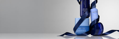 A group of blue and navy skincare products wrapped in a dark blue ribbon, set against a clean light gray studio background.