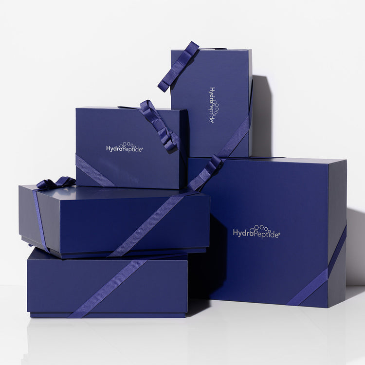 A stack of dark blue HydroPeptide gift boxes with matching ribbon handles, arranged on a clean white background.