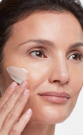 Woman applying cream to her face with a white background