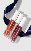 Three Perfecting Glosses with white caps on a light gray background with ribbon