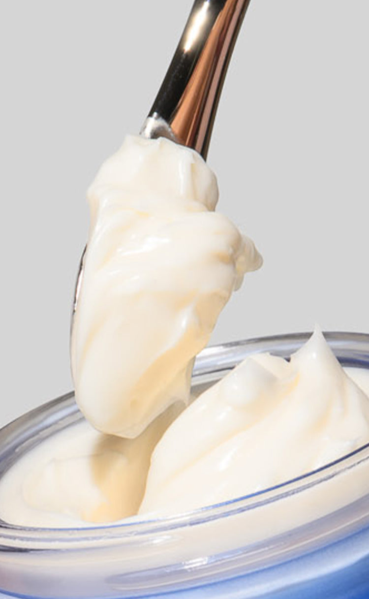 Spoon lifting a scoop of creamy Power Lift Moisturizer from a container on a gray background